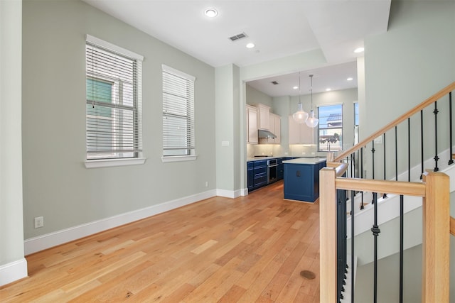 interior space featuring decorative light fixtures, a center island, a breakfast bar, light wood-type flooring, and blue cabinets