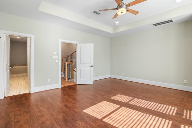 unfurnished bedroom featuring ceiling fan, ensuite bath, wood-type flooring, and a raised ceiling