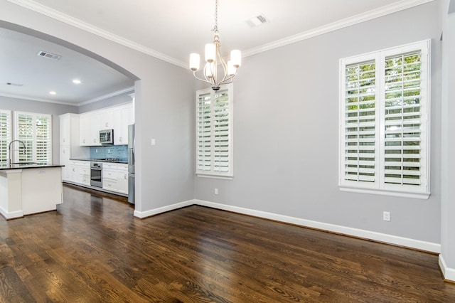 interior space featuring backsplash, pendant lighting, appliances with stainless steel finishes, ornamental molding, and white cabinets