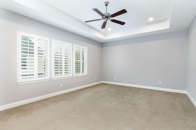 carpeted spare room featuring ceiling fan and a raised ceiling