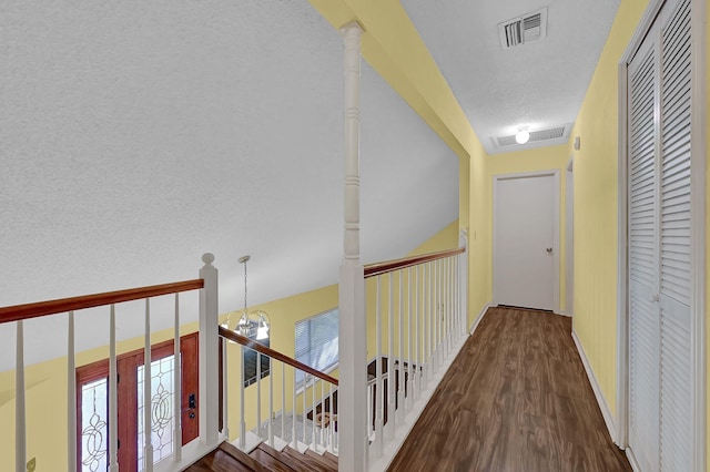 hall featuring decorative columns, hardwood / wood-style floors, a textured ceiling, and a notable chandelier