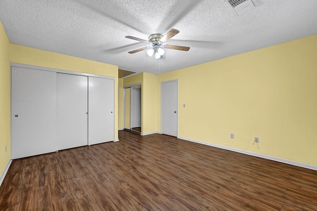 unfurnished bedroom with ceiling fan, dark hardwood / wood-style flooring, a textured ceiling, and two closets