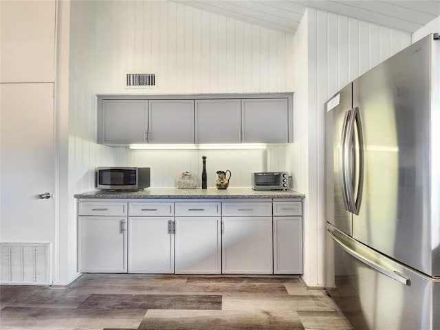 kitchen featuring gray cabinetry, wooden walls, stainless steel appliances, and hardwood / wood-style floors