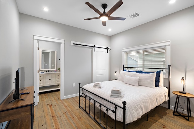 bedroom with ceiling fan, a barn door, light hardwood / wood-style floors, sink, and connected bathroom