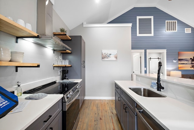 kitchen featuring appliances with stainless steel finishes, sink, wood walls, light hardwood / wood-style flooring, and range hood