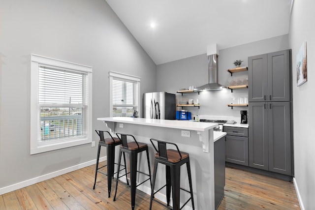 kitchen with a kitchen bar, stainless steel refrigerator, gray cabinetry, wall chimney exhaust hood, and range