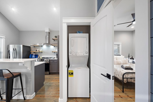 laundry room with ceiling fan, hardwood / wood-style floors, and stacked washer and clothes dryer