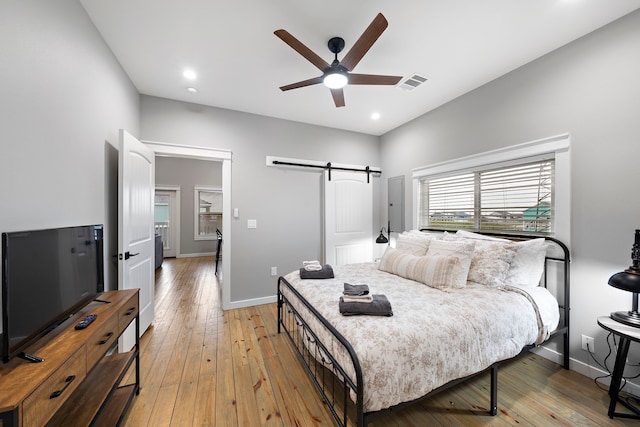 bedroom with light wood-type flooring, ceiling fan, and a barn door