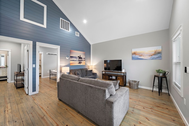 living room with high vaulted ceiling, light wood-type flooring, and wooden walls