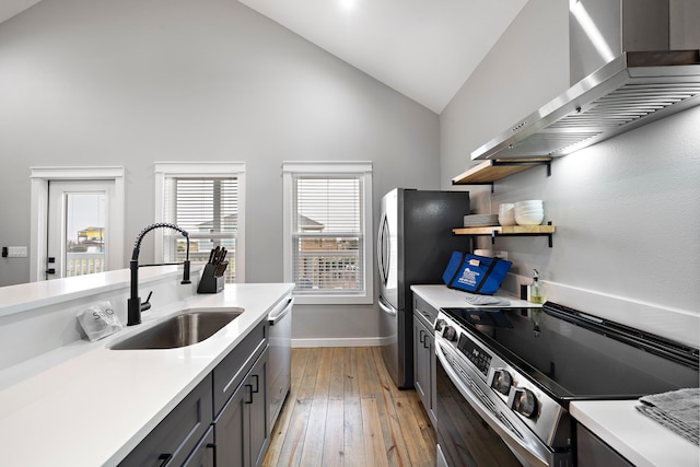 kitchen with stainless steel appliances, high vaulted ceiling, wall chimney exhaust hood, light hardwood / wood-style flooring, and sink