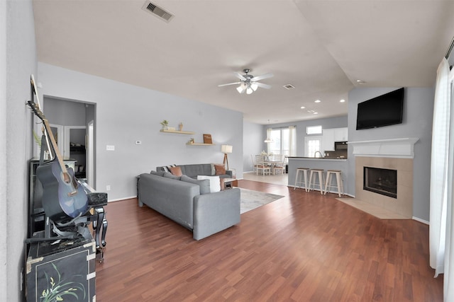 living room with vaulted ceiling, ceiling fan, wood-type flooring, and a tile fireplace