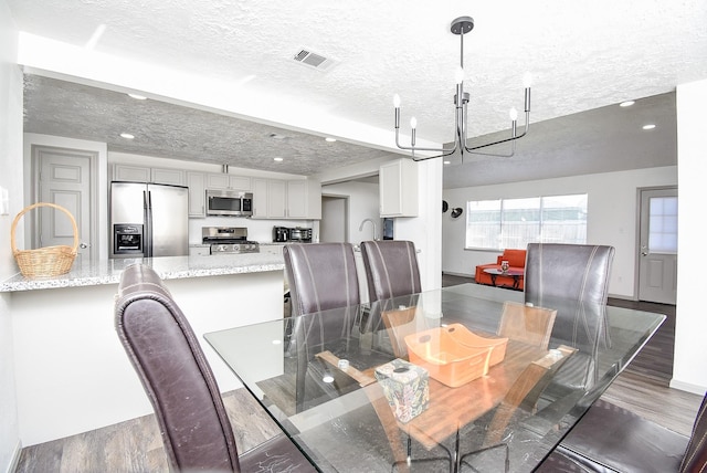 dining area featuring sink, a textured ceiling, dark hardwood / wood-style floors, and an inviting chandelier