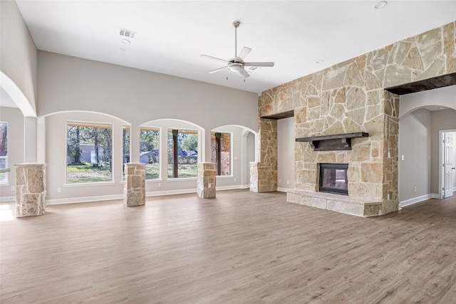 unfurnished living room featuring ceiling fan, wood-type flooring, and a stone fireplace