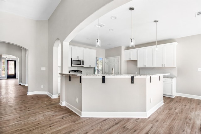 kitchen with white cabinets, a kitchen breakfast bar, light stone counters, and pendant lighting