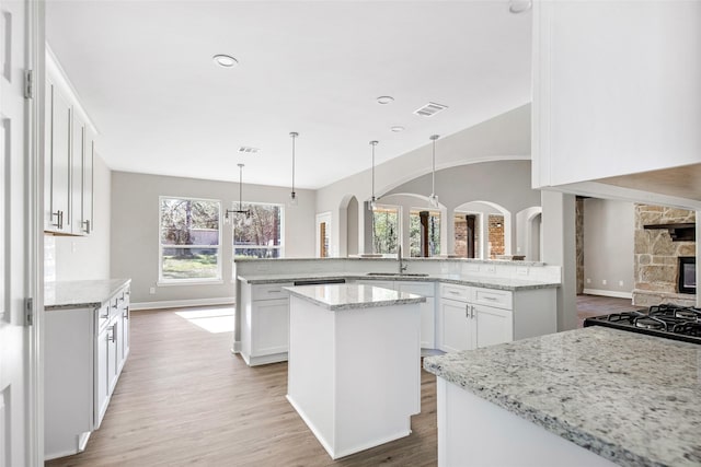 kitchen with light stone countertops, white cabinets, a kitchen island, decorative light fixtures, and kitchen peninsula