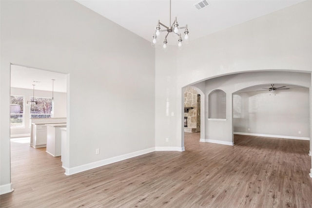 empty room featuring light wood-type flooring, ceiling fan with notable chandelier, and a towering ceiling