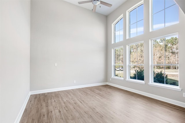 spare room with ceiling fan, a wealth of natural light, a towering ceiling, and light hardwood / wood-style flooring