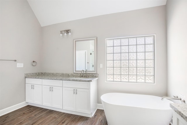 bathroom featuring hardwood / wood-style flooring, a bathtub, vanity, and vaulted ceiling