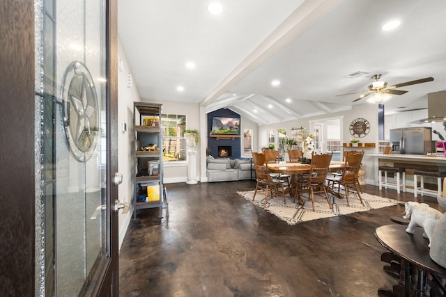 dining space featuring a fireplace, lofted ceiling with beams, concrete floors, and ceiling fan