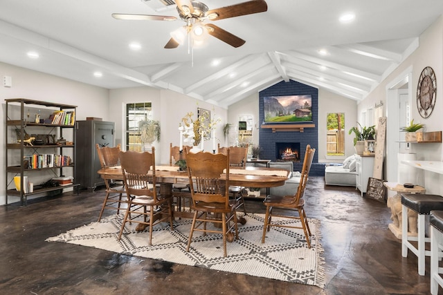 dining area featuring ceiling fan, plenty of natural light, a fireplace, and vaulted ceiling with beams