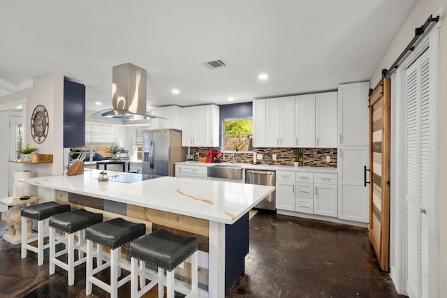 kitchen featuring sink, white cabinetry, stainless steel appliances, island range hood, and a barn door