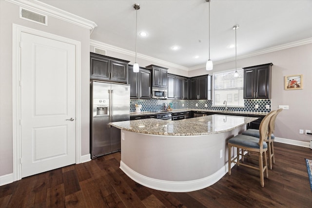 kitchen with pendant lighting, a breakfast bar, appliances with stainless steel finishes, a kitchen island, and dark hardwood / wood-style flooring