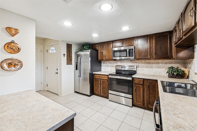 kitchen with light tile patterned floors, appliances with stainless steel finishes, backsplash, dark brown cabinets, and sink