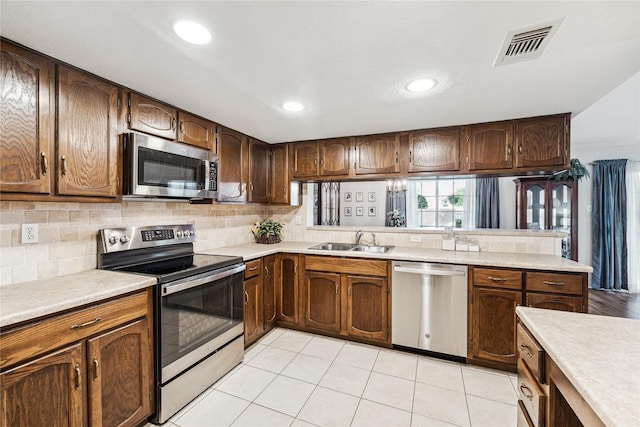 kitchen with light tile patterned floors, kitchen peninsula, stainless steel appliances, backsplash, and sink