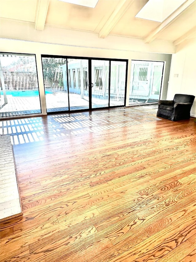 unfurnished living room featuring beamed ceiling, light wood-type flooring, and a skylight