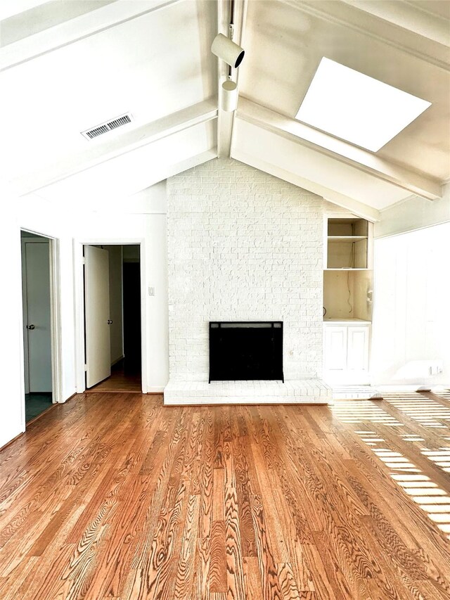 unfurnished living room with vaulted ceiling with skylight, built in shelves, hardwood / wood-style floors, and a fireplace