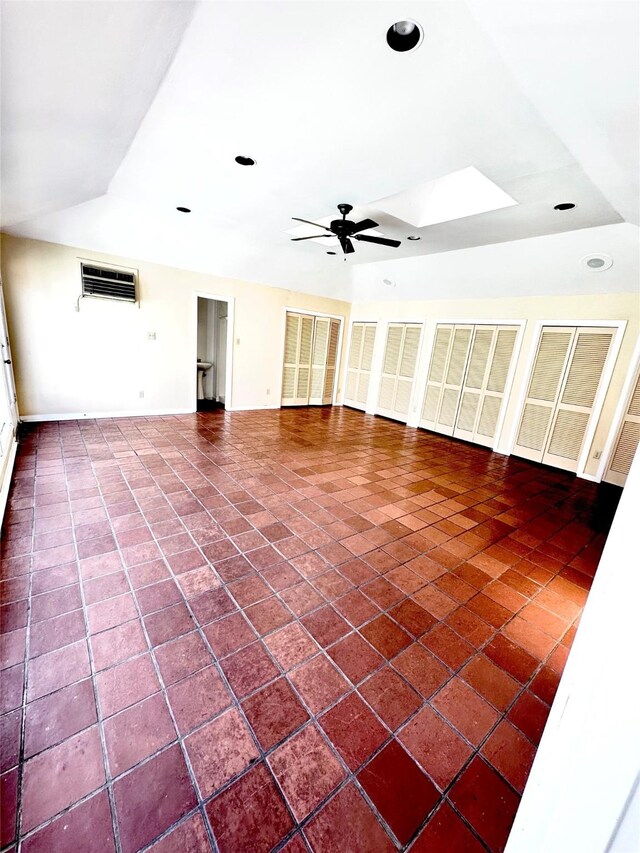 unfurnished living room featuring ceiling fan, lofted ceiling with skylight, and a wall unit AC