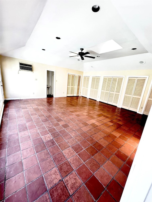 unfurnished living room with ceiling fan, a skylight, and a wall unit AC