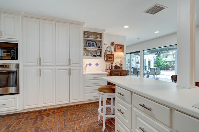 6143 Ella Lee Ln, Houston, TX 77057 - kitchen featuring brick floor, light countertops, stainless steel oven, white cabinetry, and visible vents