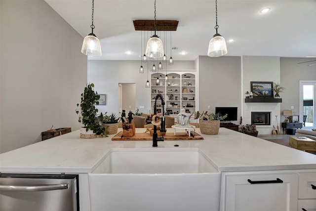 kitchen with decorative light fixtures, an island with sink, stainless steel dishwasher, and a fireplace