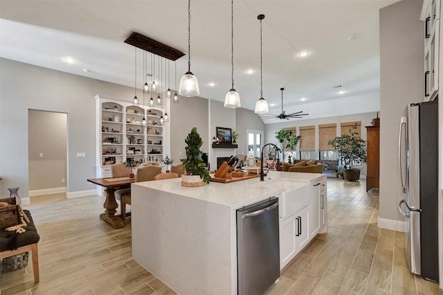 kitchen featuring ceiling fan, appliances with stainless steel finishes, a kitchen island with sink, pendant lighting, and white cabinets