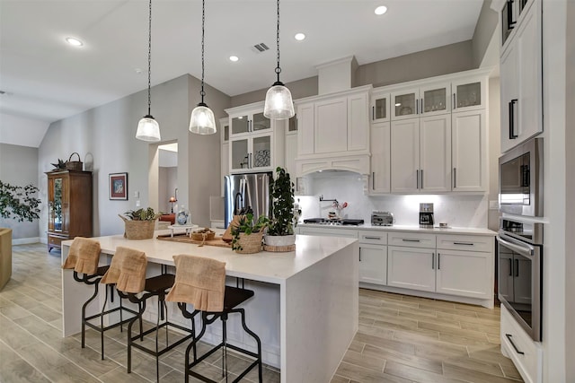 kitchen featuring a kitchen bar, decorative light fixtures, white cabinetry, stainless steel appliances, and a kitchen island with sink