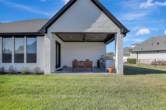 rear view of property featuring ceiling fan, exterior kitchen, a patio area, and a yard