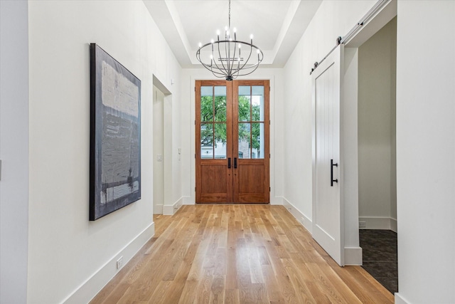 doorway with french doors, an inviting chandelier, a tray ceiling, light hardwood / wood-style flooring, and a barn door