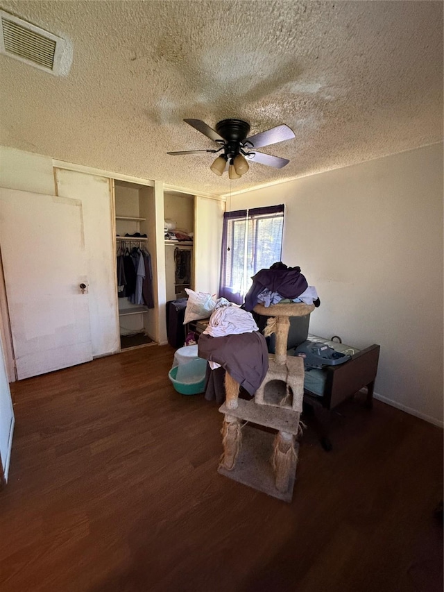 bedroom with a textured ceiling, ceiling fan, dark hardwood / wood-style floors, and multiple closets