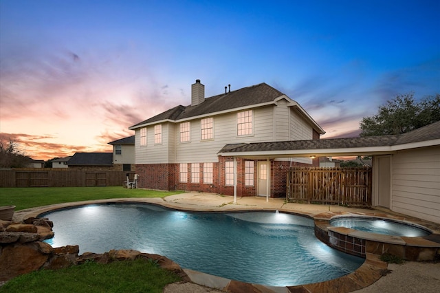 pool at dusk featuring an in ground hot tub, a lawn, and pool water feature