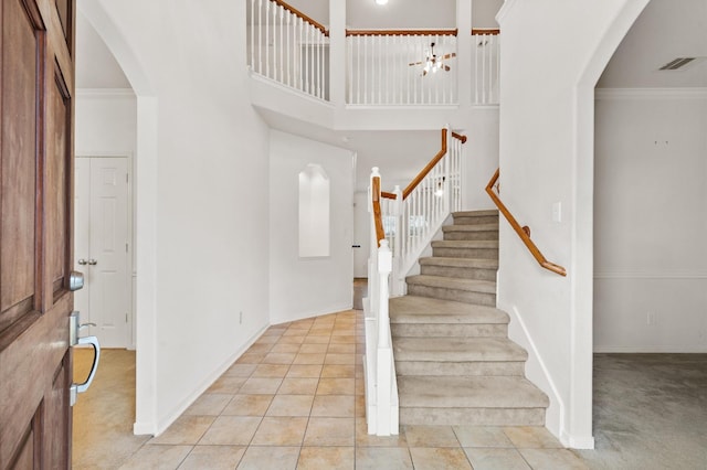 entryway featuring a towering ceiling, light tile patterned flooring, and ornamental molding