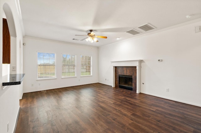 unfurnished living room with ceiling fan, a tiled fireplace, dark wood-type flooring, and crown molding