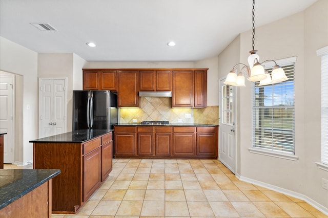 kitchen featuring tasteful backsplash, a notable chandelier, black fridge, dark stone counters, and hanging light fixtures