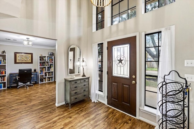 entrance foyer with crown molding, wood-type flooring, a towering ceiling, and an inviting chandelier