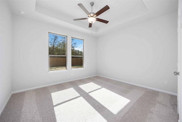 empty room featuring ceiling fan, light carpet, and a tray ceiling