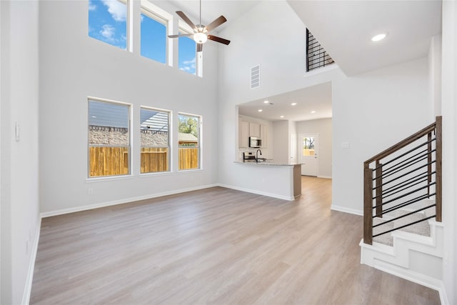 unfurnished living room featuring ceiling fan, a towering ceiling, light hardwood / wood-style flooring, and sink