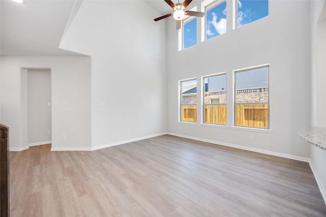 unfurnished living room featuring ceiling fan, a towering ceiling, and light hardwood / wood-style flooring