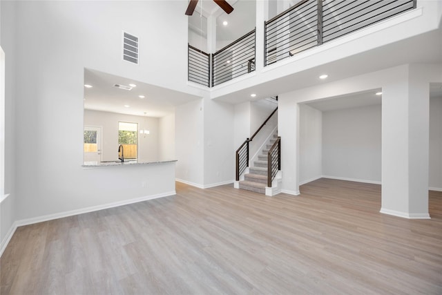 unfurnished living room featuring ceiling fan, a high ceiling, sink, and light wood-type flooring