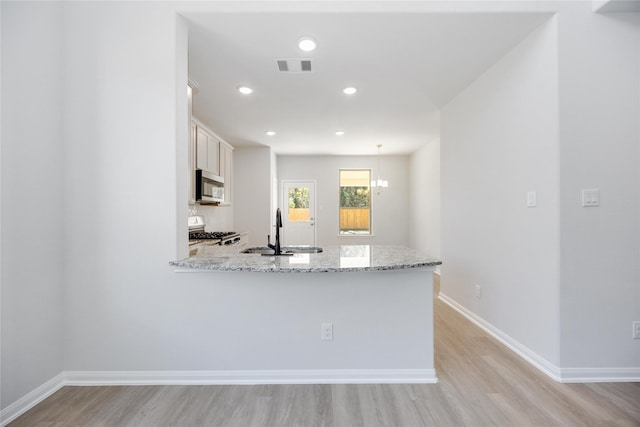 kitchen with sink, white cabinetry, light hardwood / wood-style flooring, light stone counters, and range