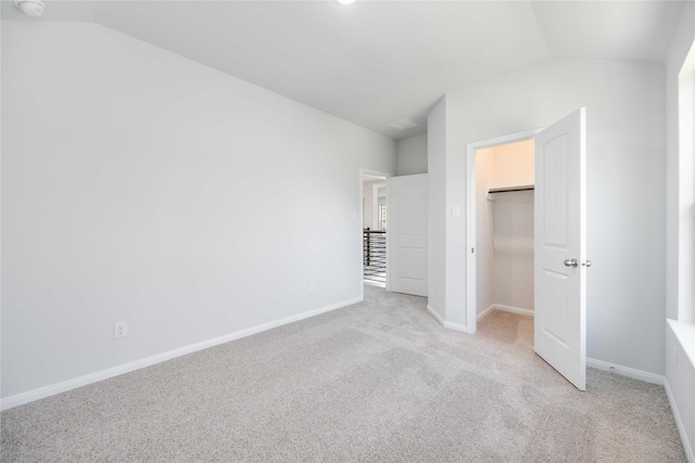 unfurnished bedroom featuring a spacious closet, light carpet, a closet, and lofted ceiling